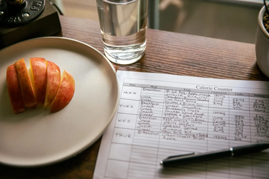 Meal plan and grocery list on a kitchen table next to a notebook