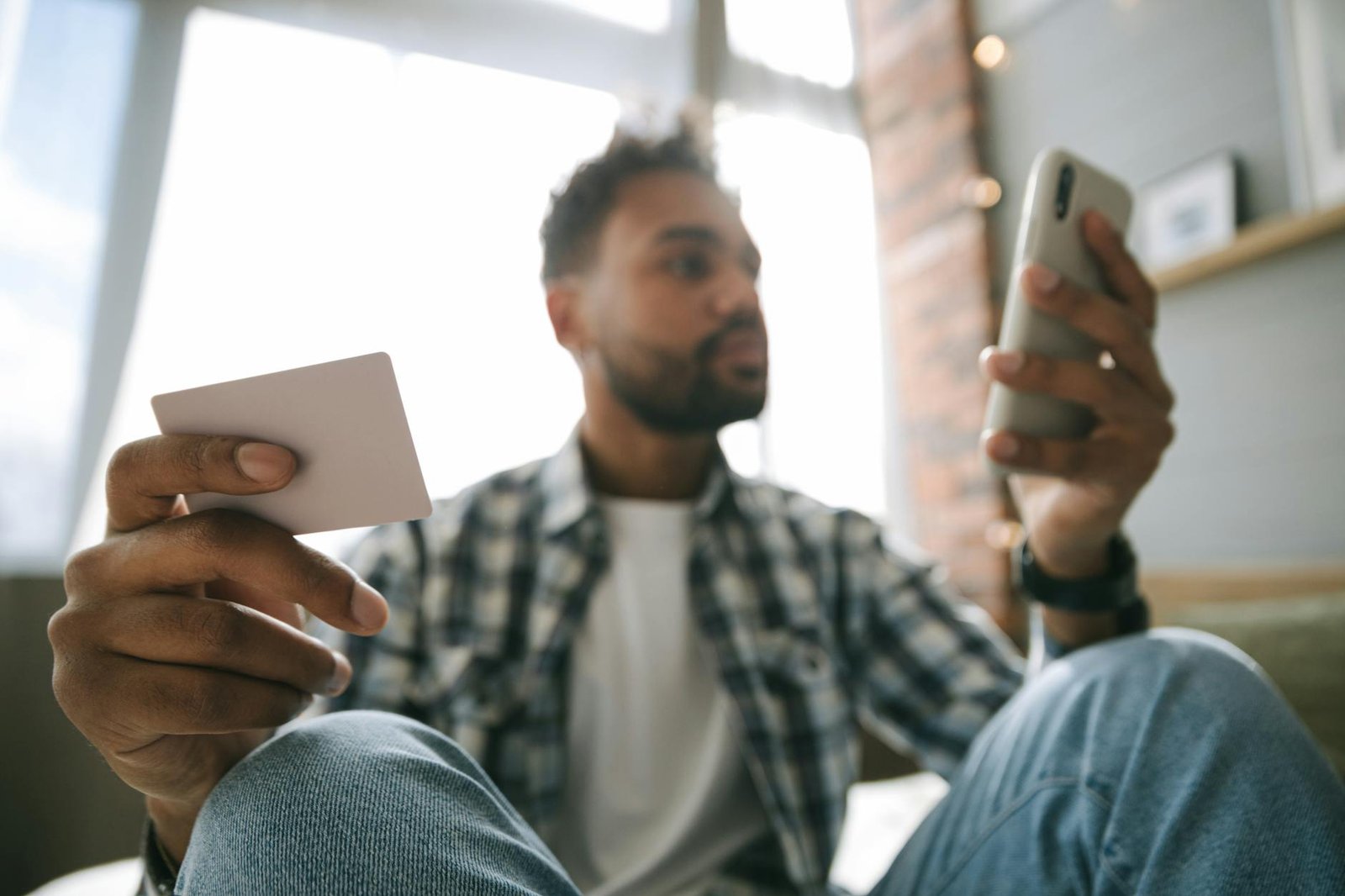 A man using a smartphone and card for online shopping in a cozy indoor setting.