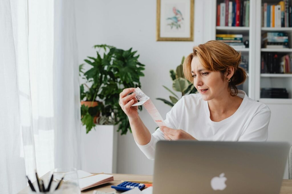 Person reviewing bills and a budget at a kitchen table, looking concerned but focused